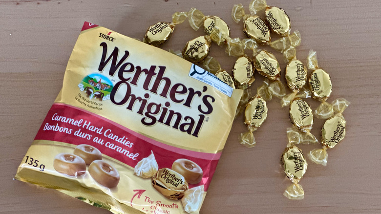 Open bag of Werther's Original Caramel Hard Candies with scattered wrapped candies on wooden table