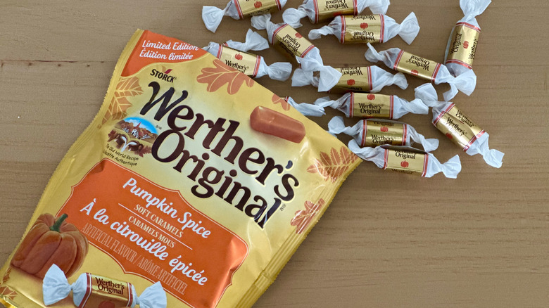 Open bag of Werther's Pumpkin Spice Caramels with scattered wrapped candies on wooden table
