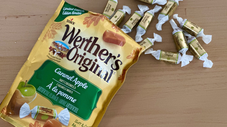 Open bag of Werther's Caramel Apple Soft Caramels with scattered wrapped candies on wooden table
