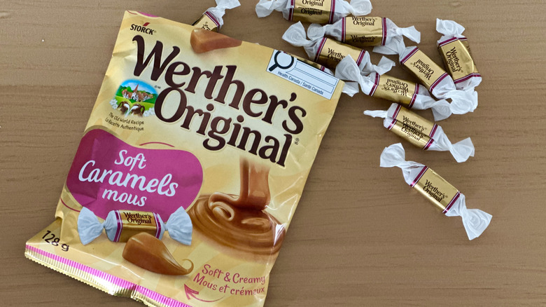 Open bag of Werther's Soft Caramels with scattered wrapped candies on wooden table