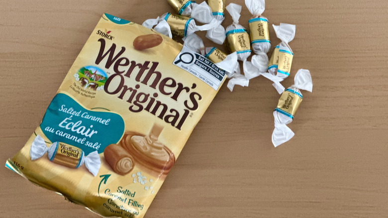 Open bag of Werther's Salted Caramel Soft Caramels with scattered wrapped candies on wooden table