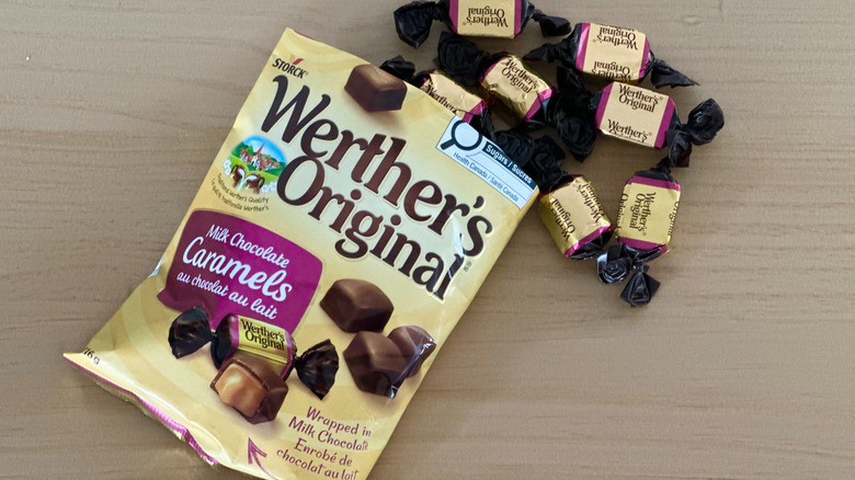 Open bag of Werther's Chocolate Covered Caramels with scattered wrapped candies on wooden table