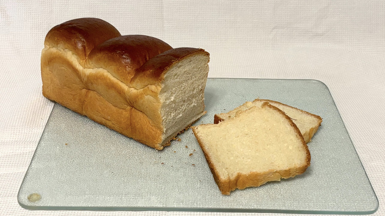 Whole Foods Japanese milk bread partially sliced on cutting board and white background