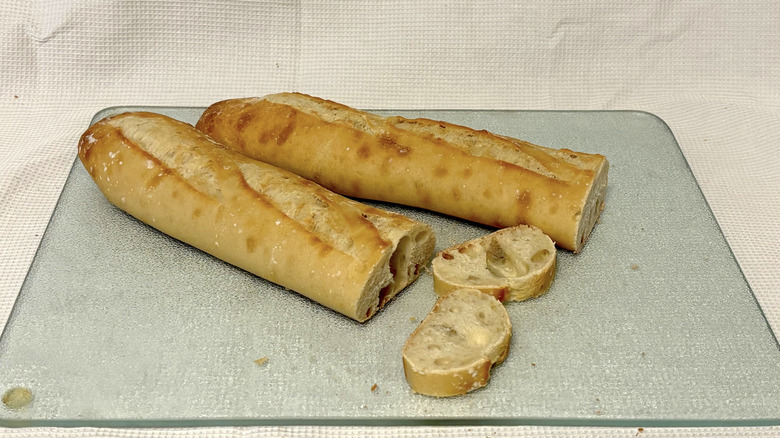 Whole Foods French baguette partially sliced on cutting board and white background