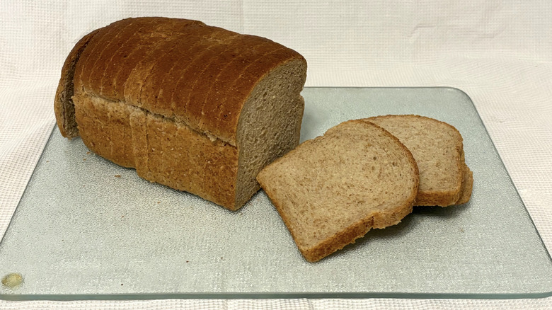 Whole Foods honey wheat pan loaf partially sliced on cutting board and white background