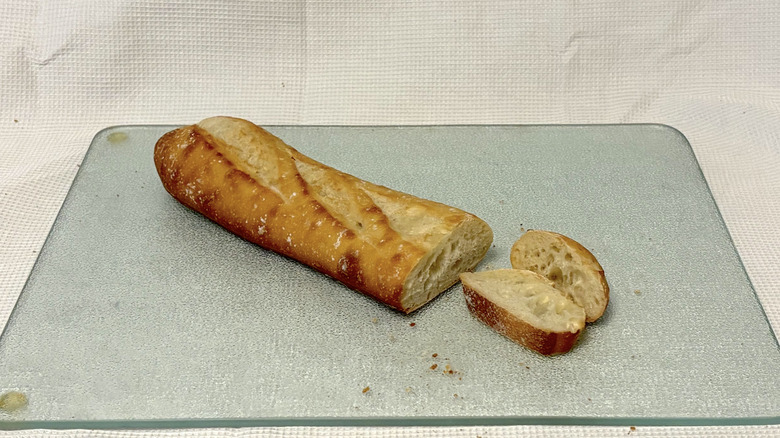 Whole Foods French demi baguette partially sliced on cutting board and white background