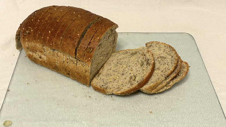 Whole Foods seeduction loaf partially sliced on cutting board and white background