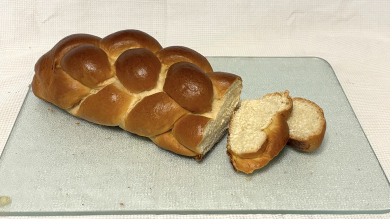 Whole Foods braided challah partially sliced on cutting board and white background
