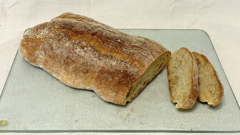 Whole Foods ciabatta partially sliced on cutting board and white background