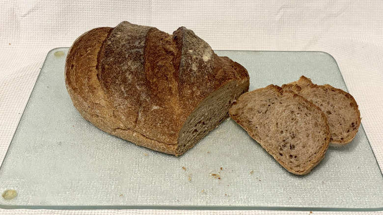 Whole Foods rustic rye bread partially sliced on cutting board and white background