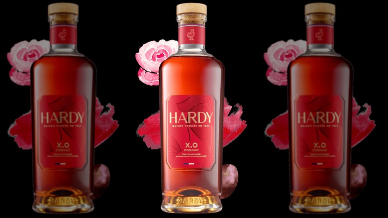 A stylized shot of Hardy XO on a plain black background with floral shapes around the bottle