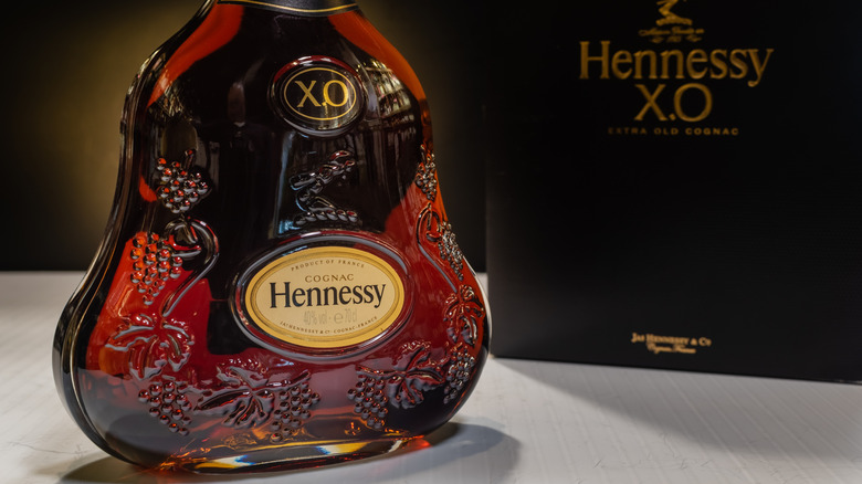 A bottle of Hennessy XO on a blank surface with its box in the background