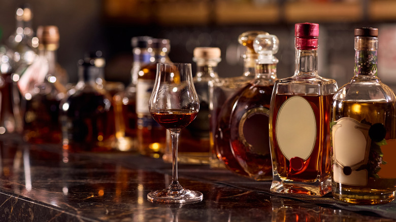A glass of brown liquor on a bar with a wide range of unbranded bottles in the background