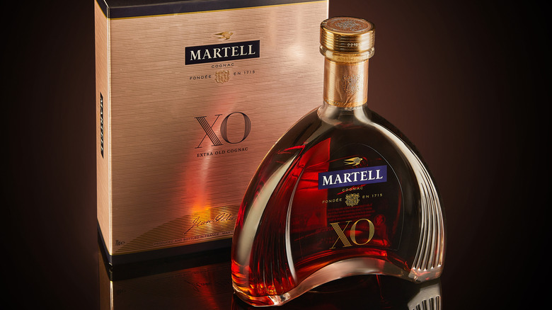 A bottle of Martell XO on a featureless dark surface with its box just behind it