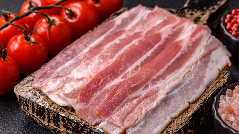 A close-up of raw bacon with tomatoes in the background