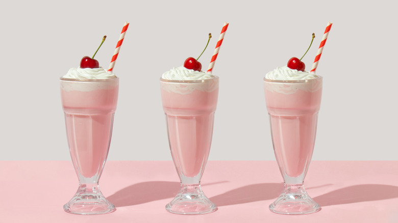 Three pink mikshakes in glass with straw, whipped cream, and cherry