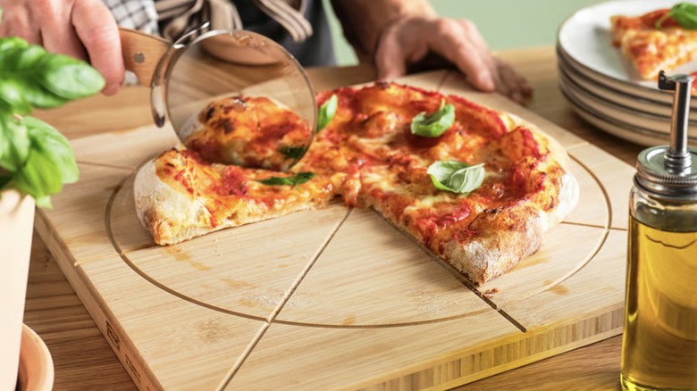 Pizza with fresh basil being cut with a pizza cutter on a notched board