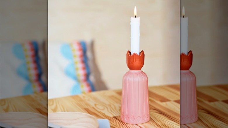 A white candle burning in a pink and red tulip-like holder