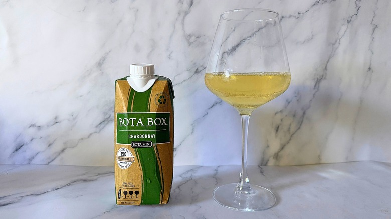Mini Bota Box Chardonnay next to wine in glass on marble surface