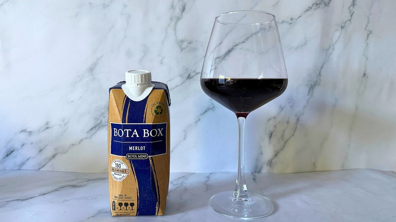 Mini Bota Box Merlot next to wine in glass on marble surface
