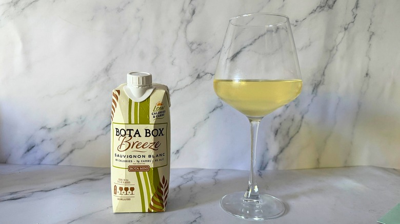 Mini Bota Box Breeze Sauvignon Blanc next to wine in glass on marble surface
