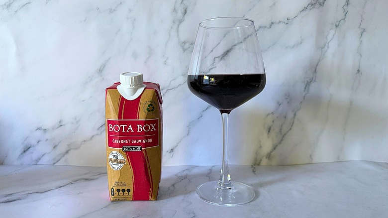 Mini Bota Box Cabernet Sauvignon next to wine in glass on marble surface