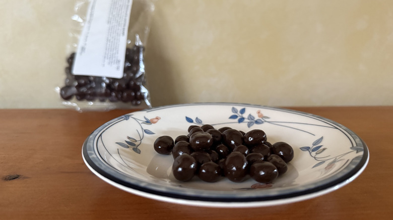 Chocolate covered coffee beans on plate in front of bag