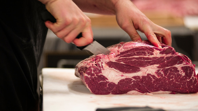A butcher cutting a piece of beef chuck on a wooden board