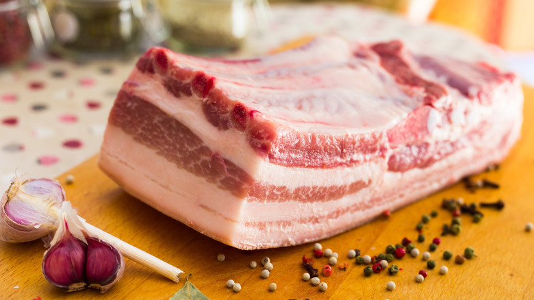 A slab of raw pork belly on a board with aromatics