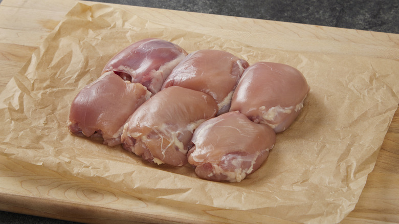 Raw boneless chicken thighs on parchment paper on cutting board