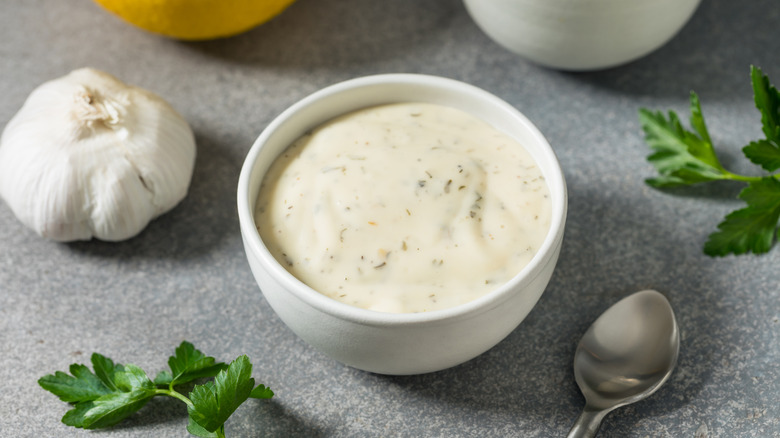 Homemade ranch dressing in white bowl next to garlic and spoon