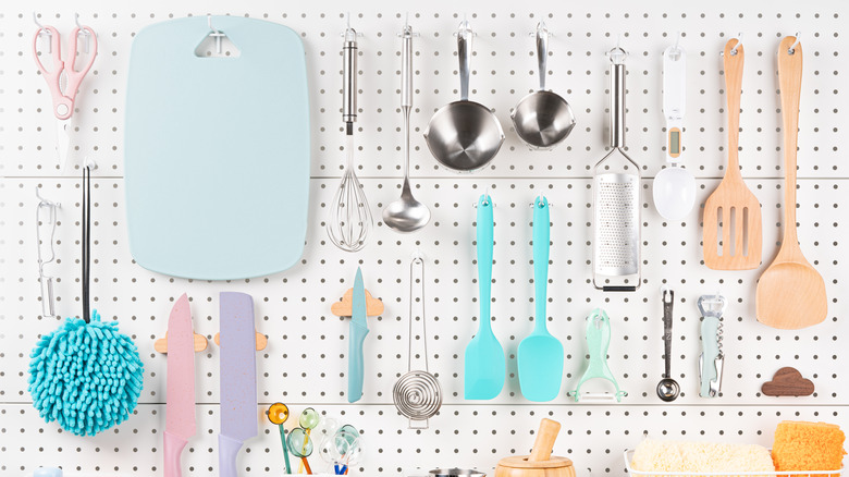 Kitchen tools including shears, cutting board, spoons, and knives hung on white peg board