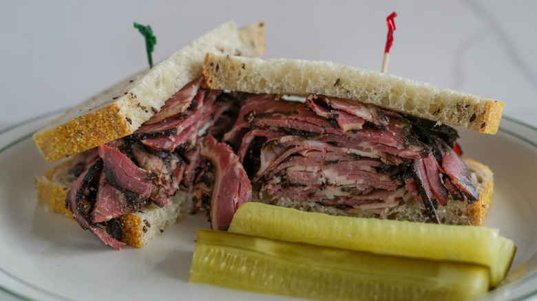 Pastrami on rye on white plate with pickle spears