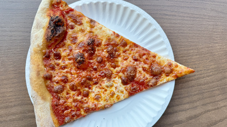 Slice of New York style pizza on white paper plate