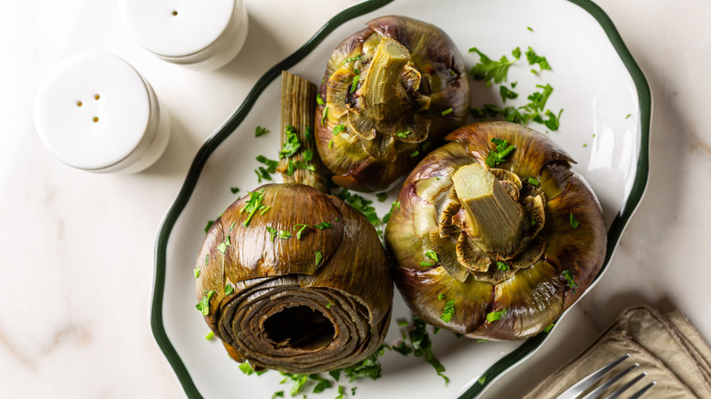 Three steamed artichokes on a white plate from the west coast
