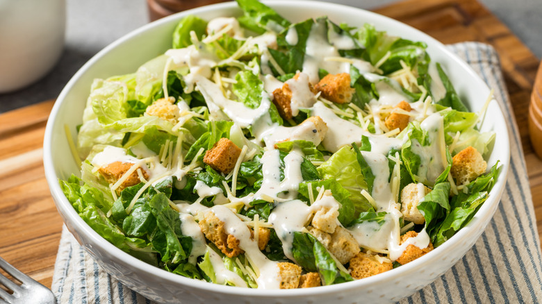 Caesar salad in white bowl on striped dish towel on wooden board