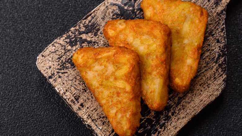 several triangular hash browns on wooden board on dark surface
