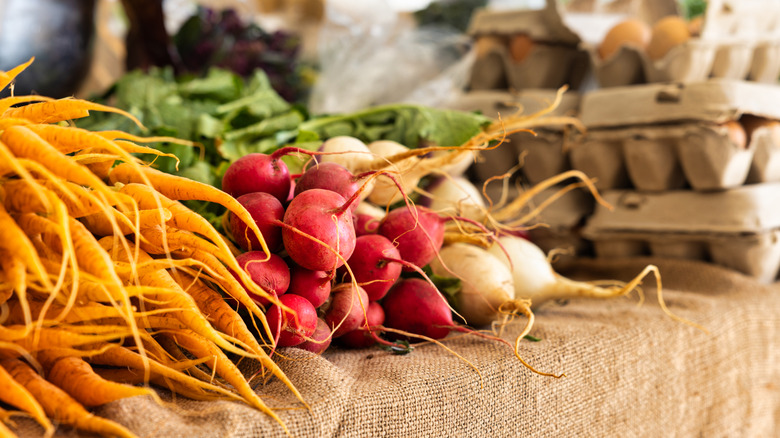 Farmer's market stall with zoomed in fresh produce including carrots, beets, and eggs