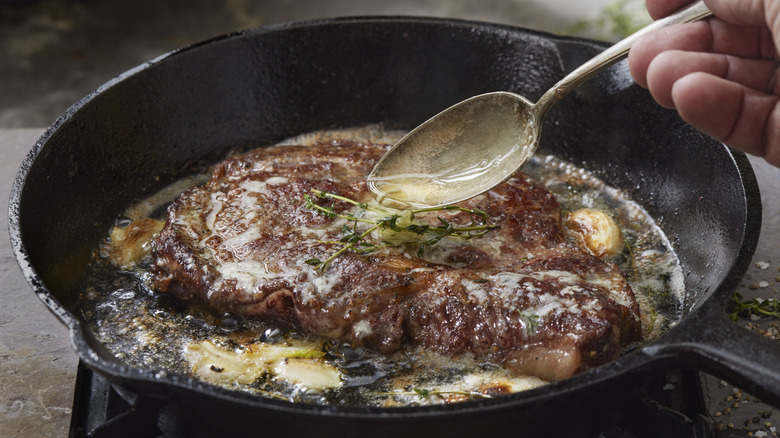A hand basting a ribeye steak with butter as it cooks in a pan