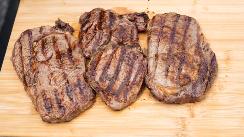 Three grilled steaks resting on a cutting board