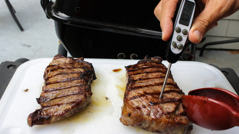 A hand sticking a kitchen thermometer into a cooked steak