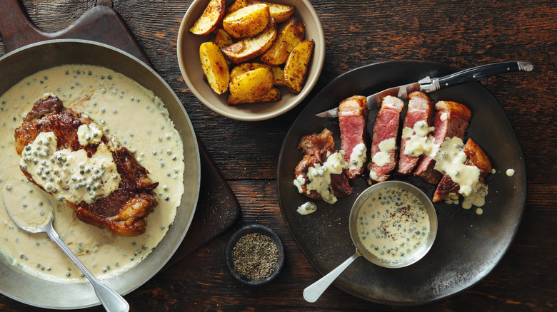 Ribeye and peppercorn sauce in a pan and served in a plate with potato wedges on the side