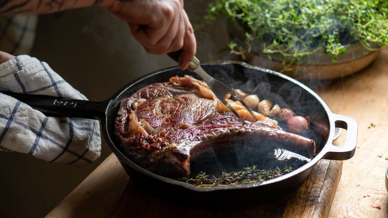 A person cooking a large steak in a cast iron pan