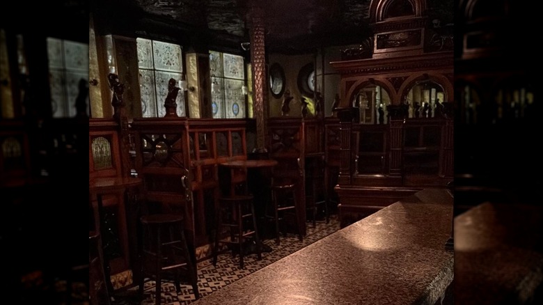 Dimly lit interior of pub with tables, chairs, and stained glass windows