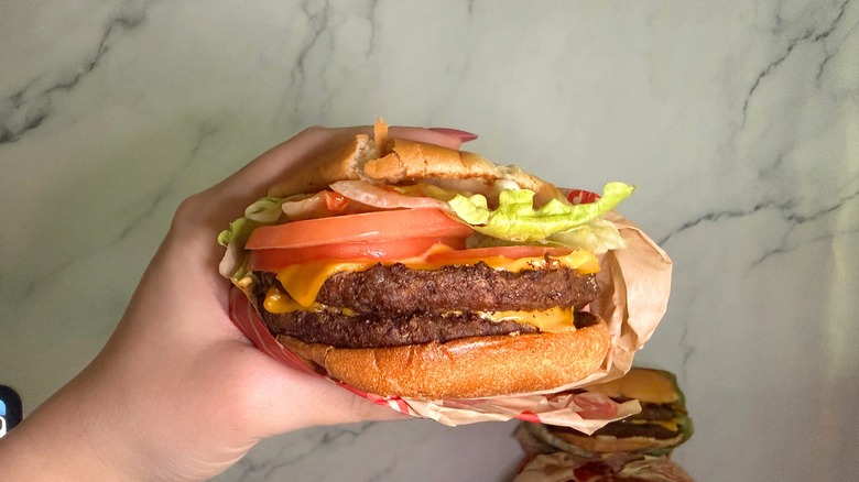 Hand holding Bacon Double Smashed Jack burger from Jack in the Box, burgers on marble surface in background