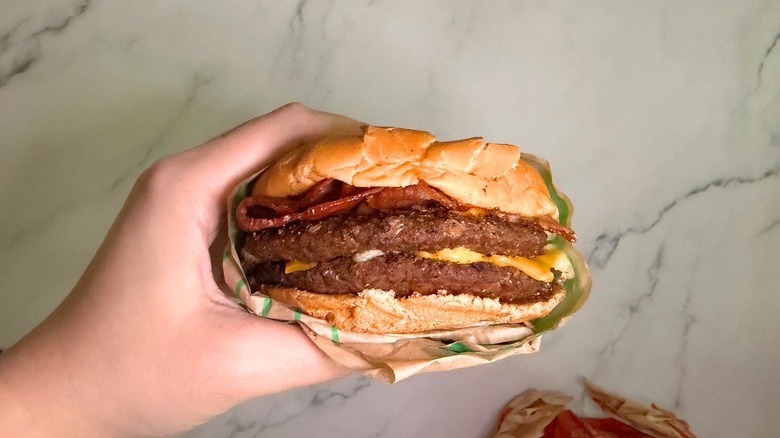 Hand holding Bacon Ultimate Cheeseburger from Jack in the Box on marble surface