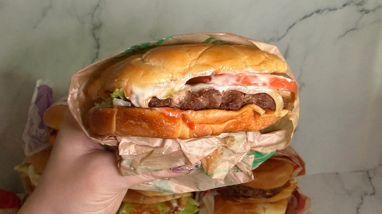 Hand holding Buttery Smashed Jack burger from Jack in the Box with burgers on marble surface in background