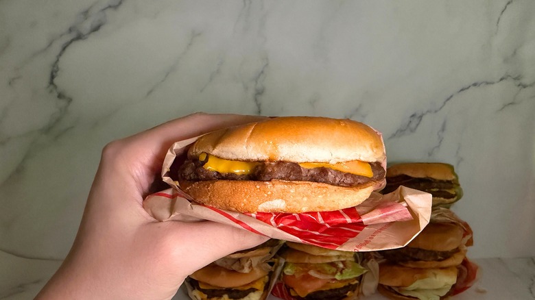 Hand holding Classic Smashed Jack burger from Jack in the Box, burgers on marble surface in background