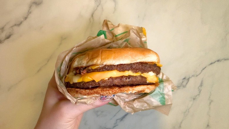Hand holding Double Jack burger from Jack in the Box on marble surface