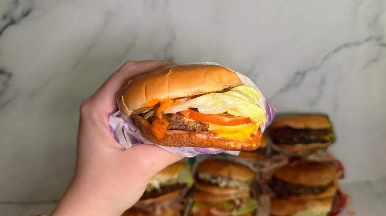 Hand holding Hot Ones Sriracha Jr. burger from Jack in the Box, burgers on marble surface in background